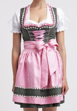 Kvinde iført en traditionel tysk dirndl kjole med en hvid bluse, grøn livdel og pink forklæde bundet med sløjfe i taljen.
