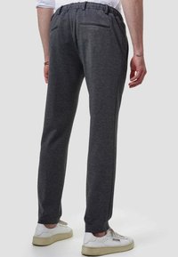 Gray, cotton sweatpants with a drawstring waistband, tapered design, and back pocket, paired with white sneakers. Texture is soft and smooth.