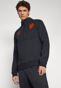 Sudadera de cremallera de color gris oscuro con el logo naranja de SF en el pecho y el swoosh de Nike. Tejido texturizado y puños y dobladillo acanalados. Corte regular.