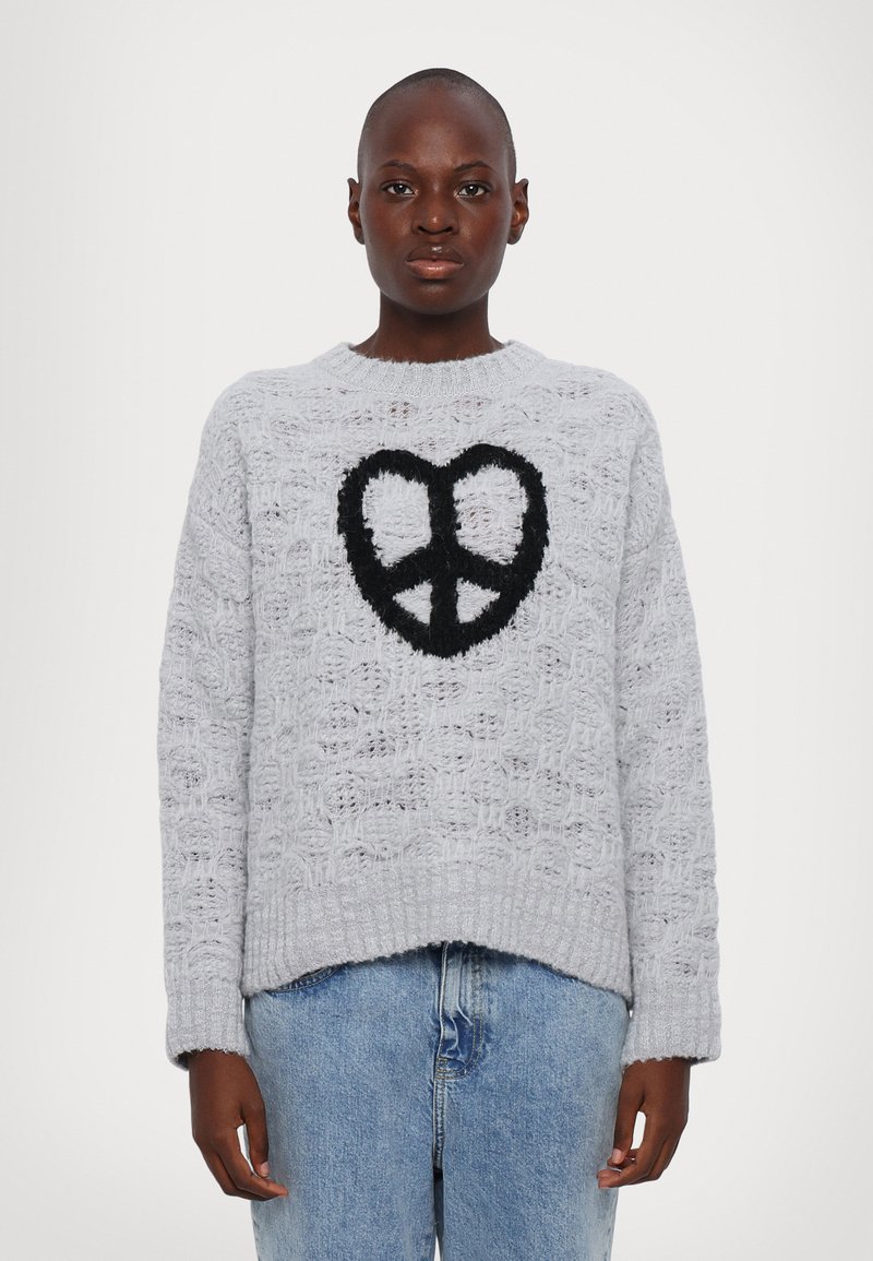 Ανοιχτό γκρίζο πλεκτό πουλόβερ με υφασμάτινη υφή και ένα μαύρο φουντωτό σύμβολο ειρήνης μπροστά. Ριμπάριστοι μανσέτες και άνετη εφαρμογή.