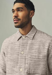 Lightweight, textured jacket in soft beige with a subtle horizontal pattern, featuring a classic collar and two front buttons.