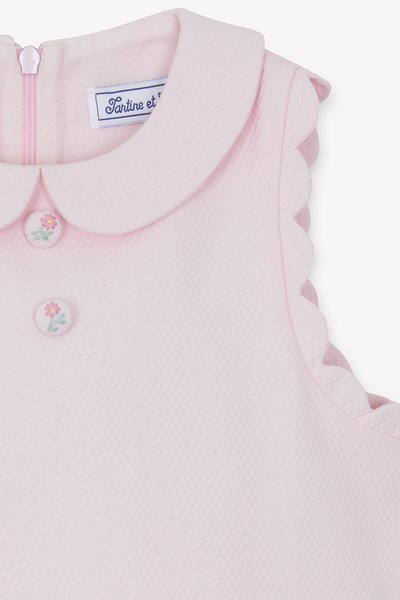 Φόρεμα ανοιχτό ροζ με υφασματική υφή, στρογγυλή γιακά, κυματιστές λεπτομέρειες στους ώμους και διακοσμητικά κουμπιά σε σχήμα λουλουδιών. Κλείσιμο με φερμουάρ στο πίσω μέρος.