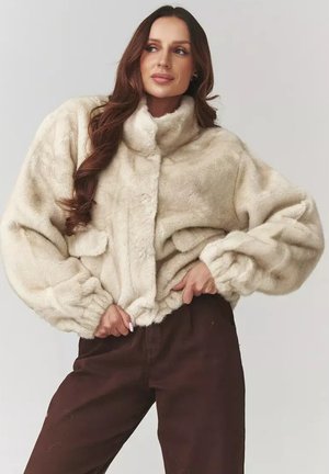 Kremowa kurtka z futra syntetycznego z wysokim kołnierzem, elastycznymi mankietami i luźnym krojem. Posiada dwie boczne kieszenie oraz zapięcie na guziki z przodu.