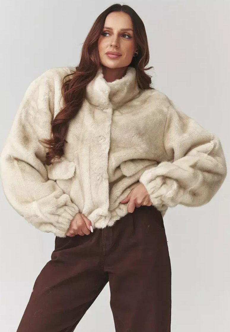 Kremowa kurtka z futra syntetycznego z wysokim kołnierzem, elastycznymi mankietami i luźnym krojem. Posiada dwie boczne kieszenie oraz zapięcie na guziki z przodu.