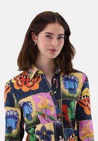 Colorful button-up shirt featuring floral and butterfly patterns in shades of orange, blue, green, and purple, with a collared neckline and soft texture.