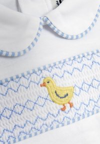 Fehér póló kék kockás gallérral és hurkolt díszítéssel. Sárga hímzett kacsa látható a mellrészen. Puha pamut anyagból készült.