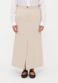 Beige linnen midiskjørt med rett silhuett, frontknapplukking, lommer i siden og en splitt foran. Brukt med svarte mesh-flats.