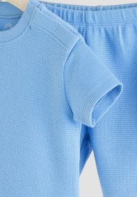 Lysblå, ribbet bomulds-t-shirt med korte ærmer, skulderknapper og matchende elastiske shorts. Glat tekstur med enkelt design.