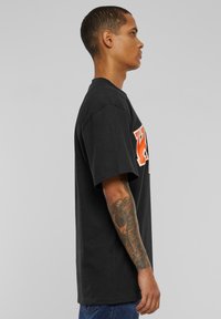 Black cotton T-shirt with short sleeves, featuring an orange graphic print on the front. Loose fit, plain design, standard crew neckline.