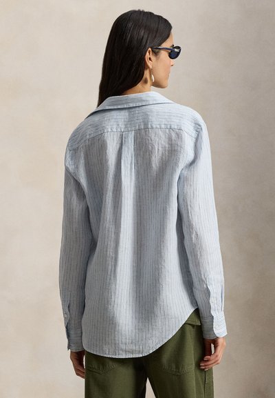 Φωτεινό γαλάζιο πουκάμισο με ρίγες, κουμπιά μπροστά, μυτερό γιακά, μακριά μανίκια και κυρτή λαιμόκοψη. Το ύφασμα φαίνεται απαλό και με υφή.