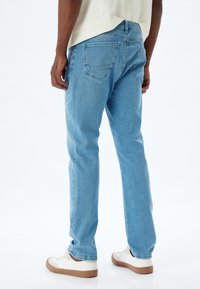 Jeans de mezclilla azul claro con corte recto, que cuentan con dos bolsillos traseros y un desgaste sutil. Llevados con zapatillas blancas y una camiseta de corte holgado.