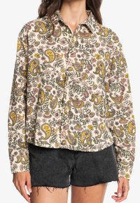 Blommönstrad skjorta med knappar i krämfärg, med paisleymönster i gult, rosa och grått. Långa ärmar med krage och avslappnad passform.