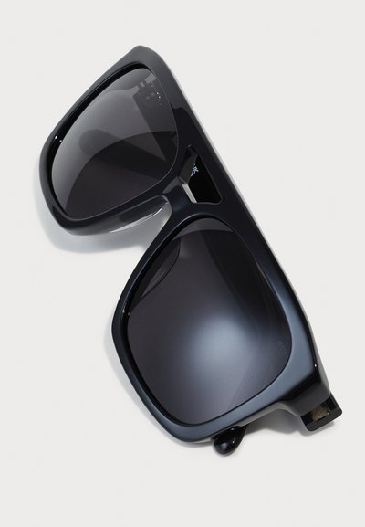 Gafas de sol negras de gran tamaño con lentes oscuros y degradados. Montura rectangular con acabado brillante y un sutil detalle de metal en la patilla.