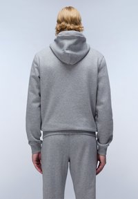 Felpa grigia in cotone con design a pullover e un grande cappuccio. Presenta polsini e orlo a coste, mostrata indossata con pantaloni coordinati.