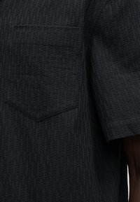 Σκούρο υφασμάτινο ύφασμα με διακριτό υφαντό σχέδιο, με μια μεγάλη ραμμένη τσέπη και κοντό μανίκι σε ένα ένδυμα.