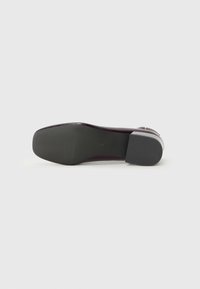Schwarzer High Heel mit glatter Sohle, ausgestattet mit einer glänzenden Oberfläche und einer kleinen Schnalle, präsentiert vor einem schlichten grauen Hintergrund.