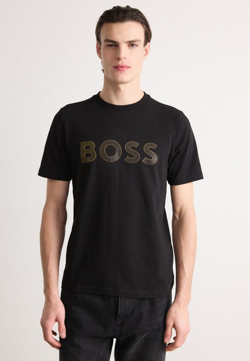Juodas medvilnės T-shirt su apvaliu kaklu, ant krūtinės spausdinamas "BOSS" aukso spalva. Trumpi rankoviai, reguliariai prigludimas.