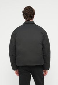 Mustahdud mustari takki, jolla on rento leikkaus, klassinen kaulus ja pehmeä rakenne, nähtynä takaa ilman näkyvää kiinnitystä tai yksityiskohtia.