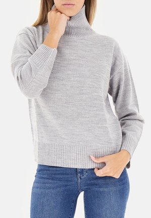Maglione grigio a collo alto con una vestibilità ampia, caratterizzato da maniche lunghe e un tessuto texture. Indossato sopra jeans blu.