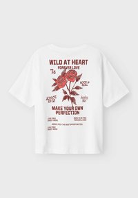 Balta kokvilnas T-kreklu ar īsām piedurknēm, kurā ir sarkani grafiski teksti un rožu ilustrācijas. Teksta fragmenti ietver "Savvaļā sirdī" un "Radiet savu izcilību."