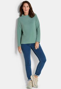Groene lange mouw, geribbelde top gecombineerd met blauwe skinny jeans en beige sneakers, met een ontspannen pasvorm en ronde hals.