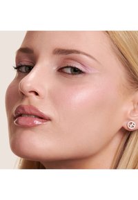 Gros plan sur un visage avec une peau lisse, un fard à paupières rose subtil, des lèvres nudes brillantes et une boucle d'oreille en forme de cercle avec un accent en strass.