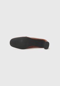 Brown leather shoe with a rounded toe, rubber sole, and a low black heel. The sole features a textured pattern for grip.