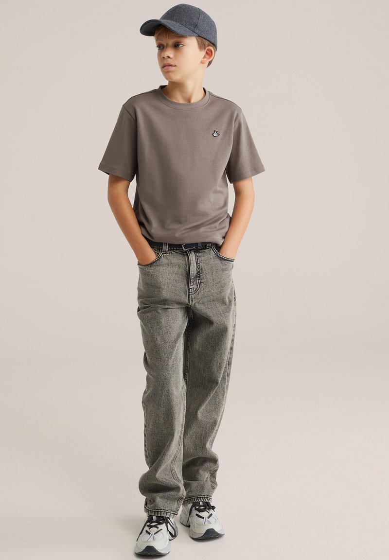 T-shirt grigia, jeans di jeans grigi a taglio largo e cappellino grigio. Scarpe da ginnastica con dettagli neri. Design semplice, vestibilità casual e tessuto morbido.