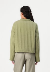 Veste matelassée verte courte avec une finition texturée, longueur cropped, et un col simple. Portée sur un pantalon de couleur claire.