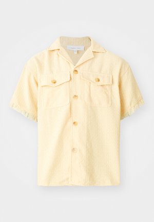 Short-sleeve, yellow shirt made of textured fabric. Features two chest pockets, button-up front, and fringe detail on sleeves.