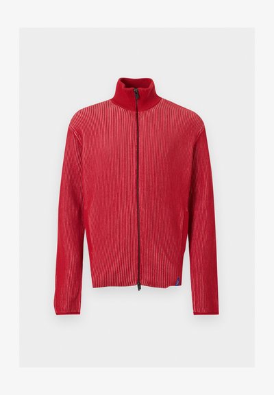 Κόκκινο ριμπ πλεκτό πουλόβερ με φερμουάρ, ψηλό γιακά και μακριά μανίκια, εμφανίζεται μπροστά σε απλό φωτεινό φόντο.