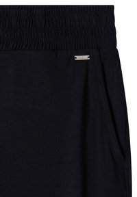 Pantalon noir avec taille élastique, poche latérale et petite étiquette métallique rectangulaire de la marque près de la poche.