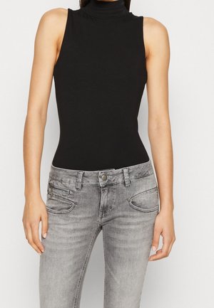 Czarny top bez rękawów z podwyższonym kołnierzem w połączeniu z jasnoszarymi, wyblakłymi dżinsami z przodu zapinanymi na zamek i guzik oraz wieloma kieszeniami.