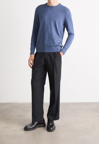 Granatowy sweter z okrągłym dekoltem z miękkiego materiału, w połączeniu z czarnymi, szerokimi spodniami i czarnymi skórzanymi butami. Prosty design, bez widocznych wzorów.