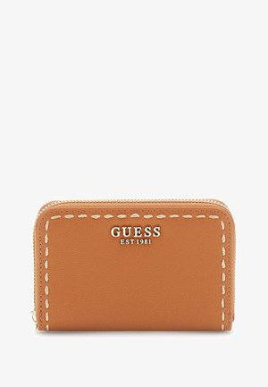 Portafoglio zip in pelle color cuoio con cuciture bianche. Presenta il logo "GUESS EST 1981" in finitura metallica sul davanti. Design compatto e rettangolare.