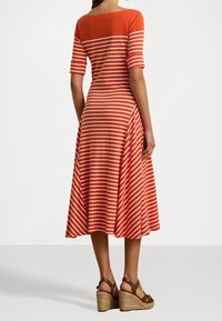 Punainen ja valkoinen raidallinen polvimittainen mekko, jossa on lyhyet hihat, mukautettu vartalo-osa ja levenevä hameosa. Yhdistetty ruskeisiin korkokenkiin.