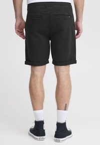 Shorts noirs avec une coupe décontractée, ourlets roulés et poches arrière. Portés avec des baskets noires et des chaussettes blanches.