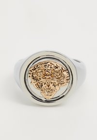 Anello color argento con un design centrale di una testa di leone dorata in evidenza, circondato da una banda circolare liscia.