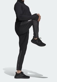 Svart atletisk outfit med långa ärmar och tapered byxor, tillverkad av slätt, lättviktigt tyg med kontrasterande mörka detaljer och texturerade skor.