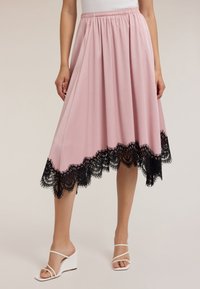 Gonna midi rosa con orlo in pizzo nero, dotata di una vita elastica arricciata e tessuto morbido. Indossata con sandali con zeppa bianchi.