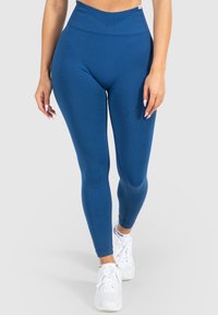 Blaue hochtaillierte Leggings mit glatter Textur, die ein figurbetontes Design und dezente Nahtdetails aufweisen, kombiniert mit weißen Sportschuhen.