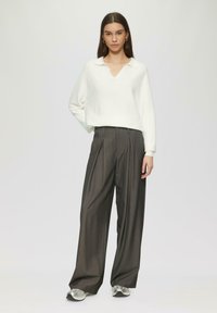 Witte geribbelde trui met een V-hals, gecombineerd met hoge taille, wijdvallende donkere gestreepte broek en zilveren sneakers.