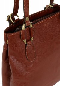 Bruine leren handtas met een gestructureerde afwerking, featuring messing hardware en korte, dubbele handvatten. Ritssluiting aan de bovenkant.