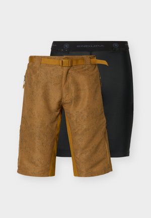 Ruskeat teksturoidut polvipituudet shortsit, joissa on sisäänrakennettu vyö, päällekkäin mustien puristushousujen kanssa, joissa on "ENDURA"-vyötteen merkintä.