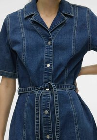 Denimklänning med krage, korta ärmar och bälte i midjan. Har kontrasterande sömmar och metallknappar framtill. Djupt blå färg.
