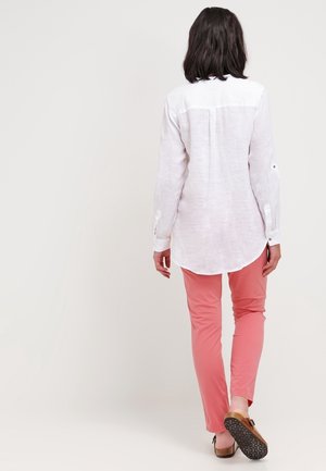 Wit linnen overhemd met lange mouwen en knoopmanchetten, gecombineerd met aansluitende roze broek. Soepele textuur en casual ontwerp.