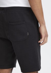Pantalones cortos de algodón negros con un corte relajado, que cuentan con un bolsillo trasero, detalles cosidos y una etiqueta de marca visible en el lateral.