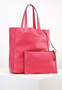 Sac fourre-tout en cuir rose avec double poignée et surface texturée, accompagné d'une pochette zippée assortie, toutes deux ornées d'accents noirs élégants.