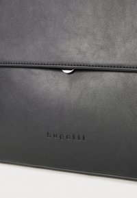 Čierna kožená taška so hladkou textúrou, vybavená strieborným zapínaním na cvok a s embosovaným logom "bugatti" na prednej strane. Jednoduchý a elegantný dizajn.