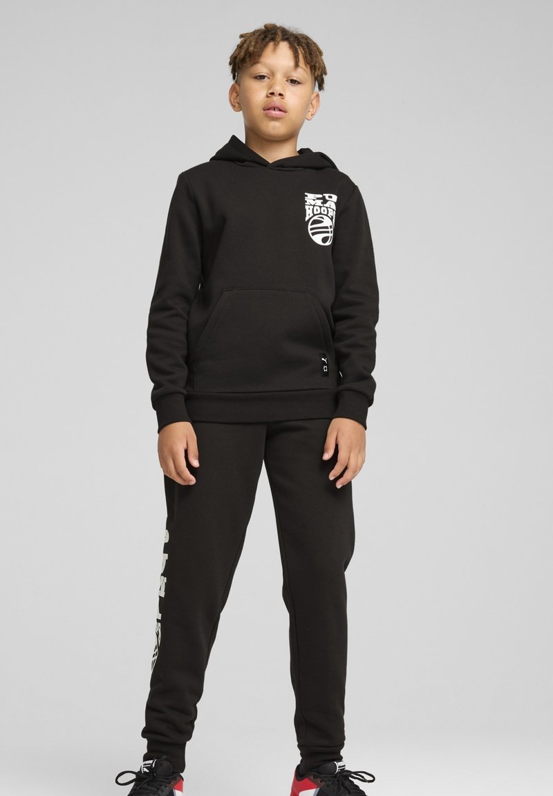 Juodas treningas su priekiu kišene, logotipu ant krūtinės ir derančiais juodais kelniais. Medžiaga turi lygų paviršių, su elastingais rankovėmis ir liemeniu.